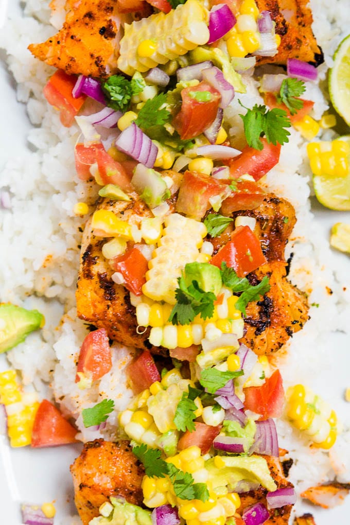 A plate of blackened cod with avocado corn salsa with tomatoes and cilantro.