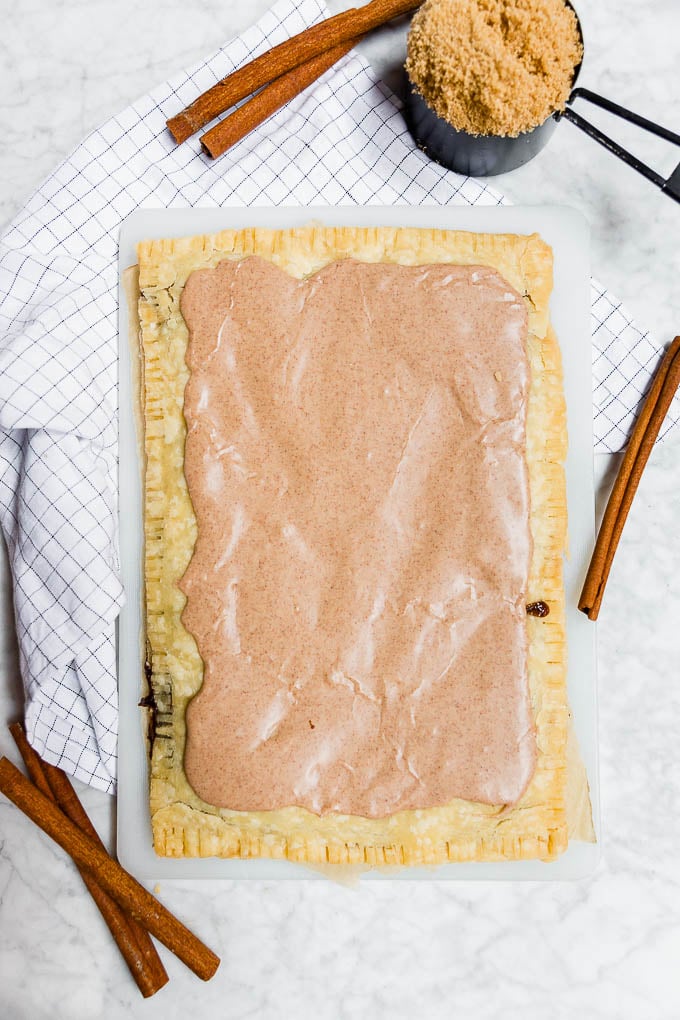 A giant sized gluten-free vegan brown sugar cinnamon pop tart with cinnamon sticks and a cup of brown sugar.