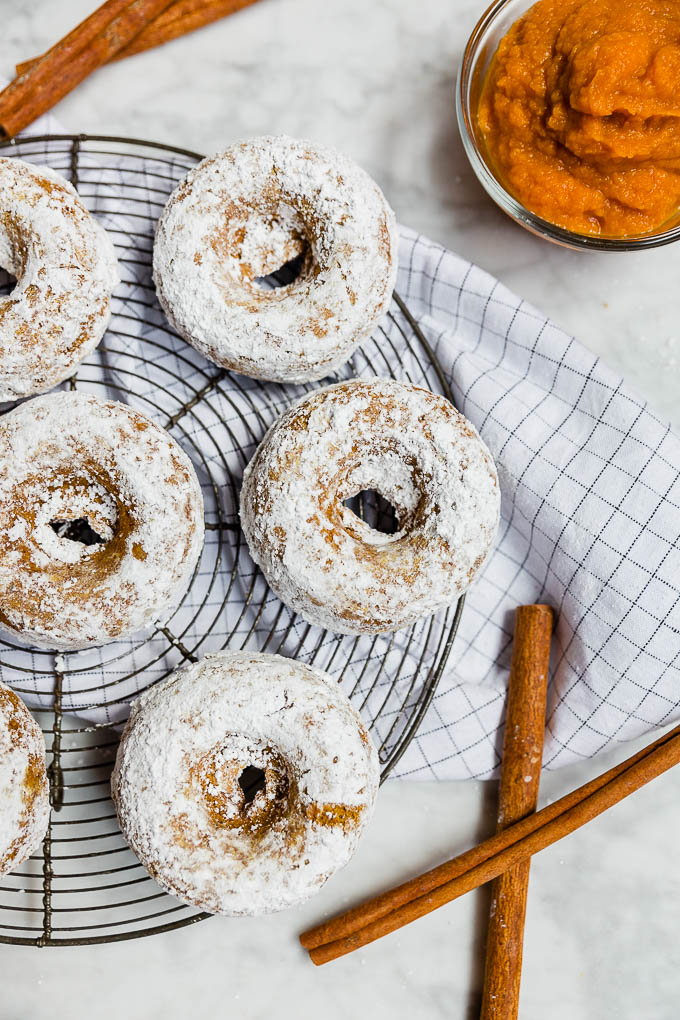 Baked pumpkin donuts rolled in powdered sugar with cinnamon sticks and pumpkin puree.