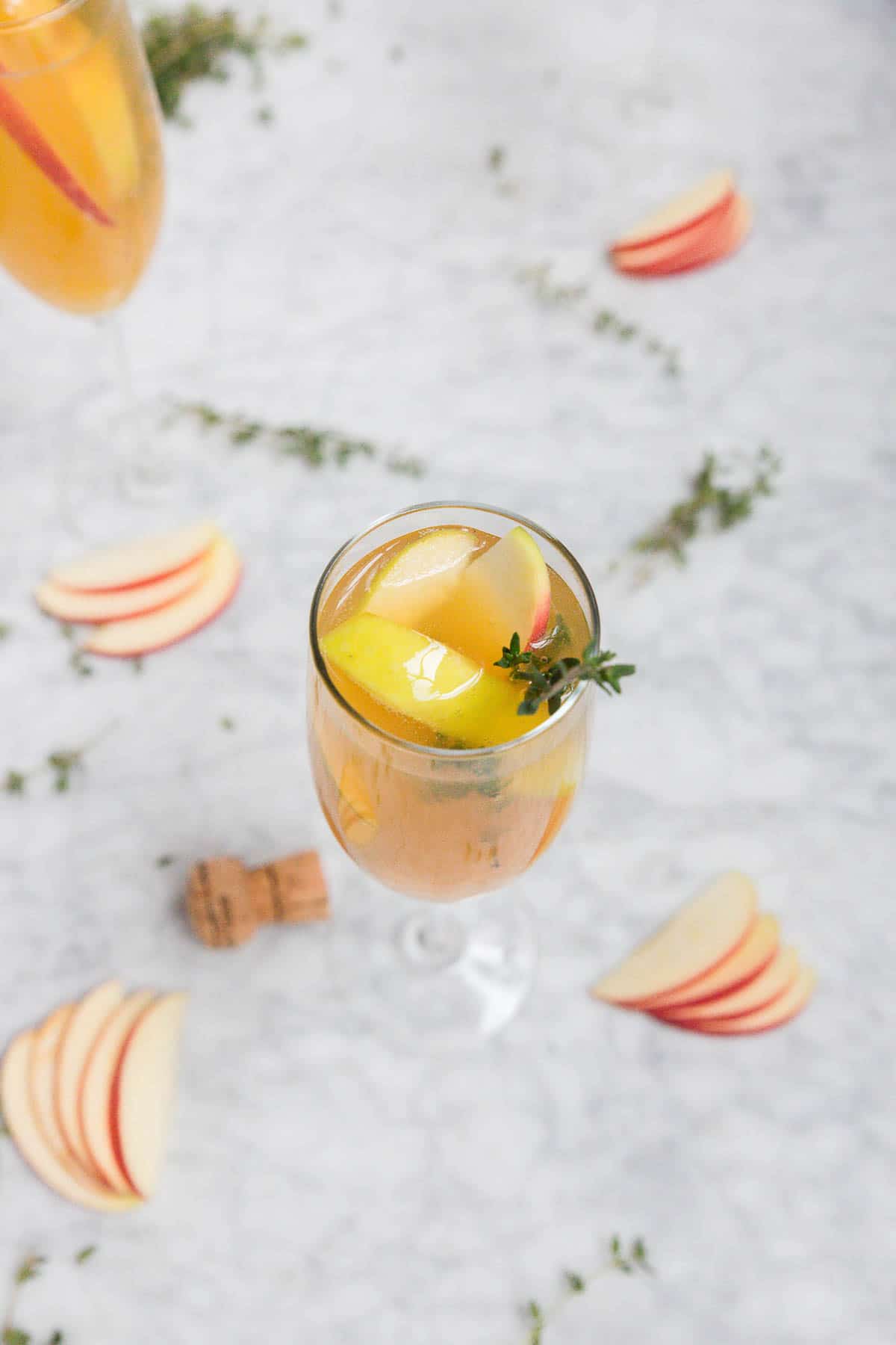 A glass of apple cider thyme mimosa cocktail with fresh apples and thyme sprigs