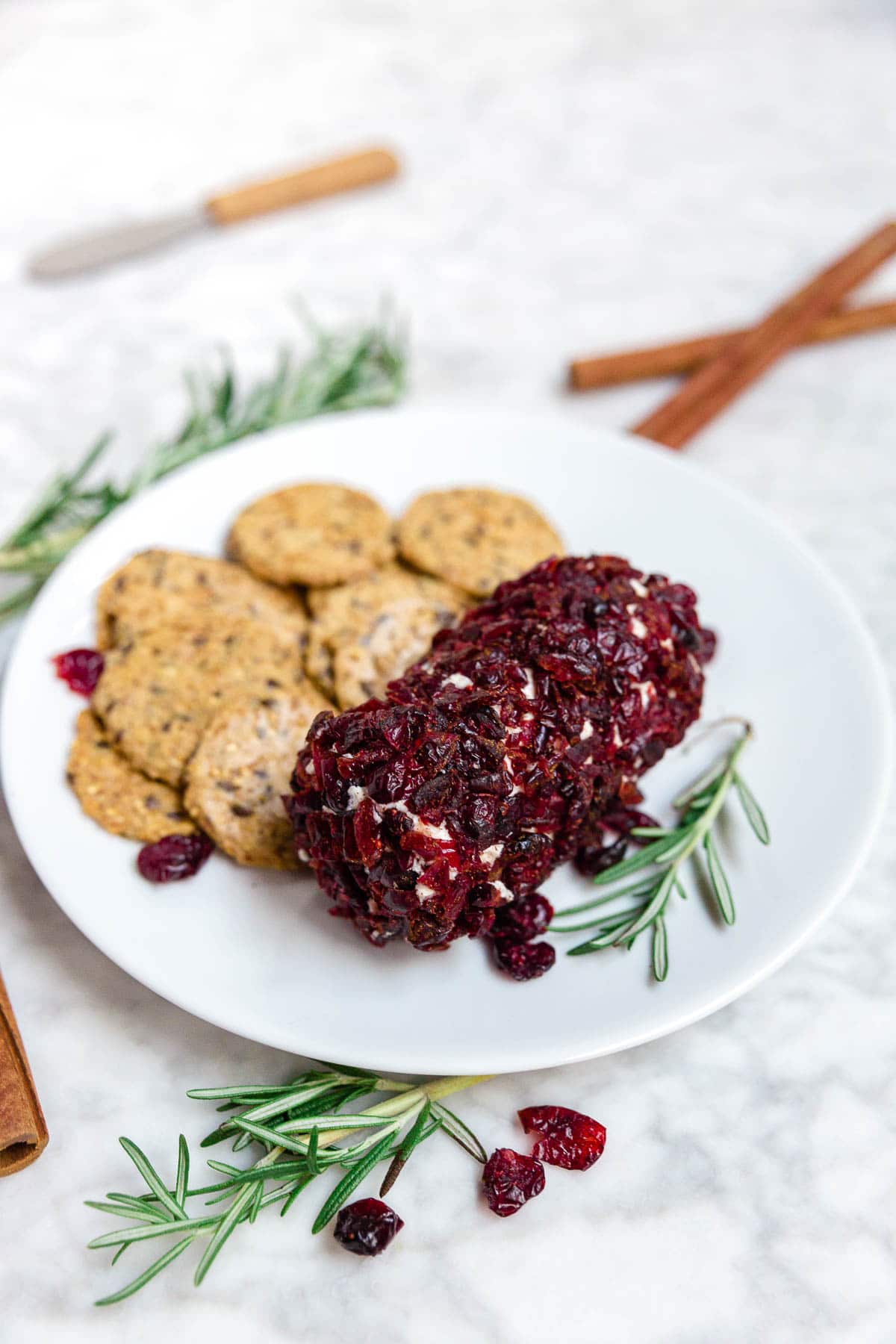 A plate with cranberry cinnamon goat cheese log and cinnamon sticks.