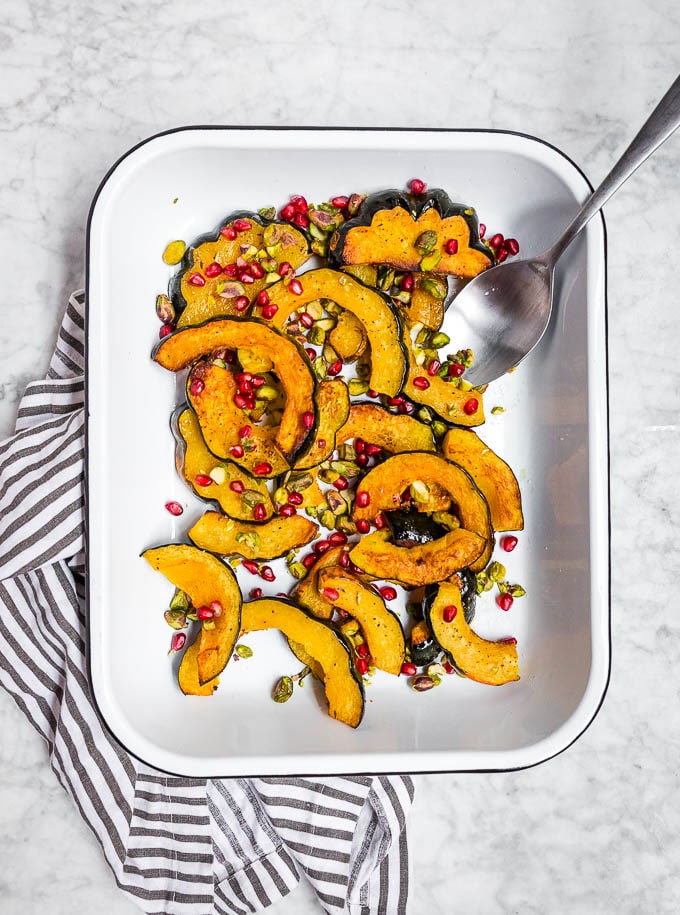 A white sheet pan with slices of acorn squash roasted with pistachios and pomegranate.