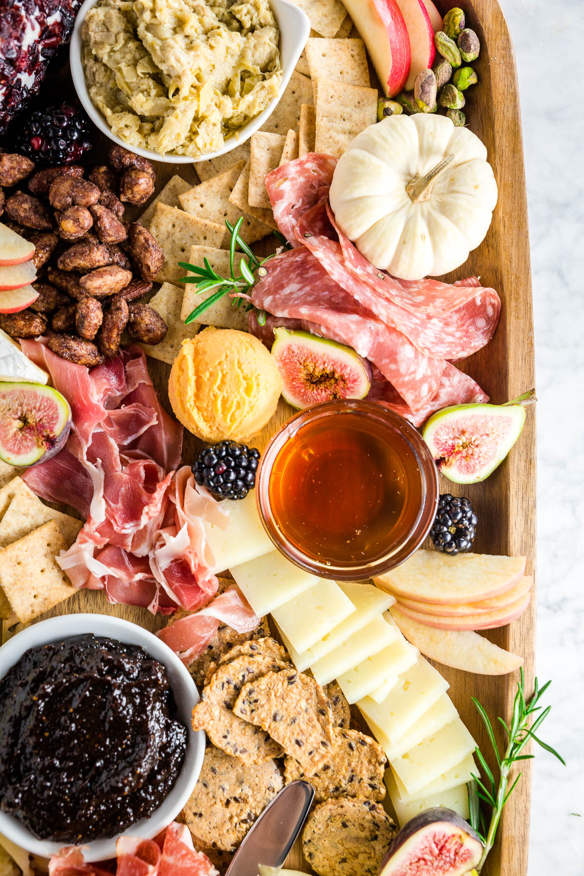 A wooden cheese board with gluten-free meats, cheeses and crackers.