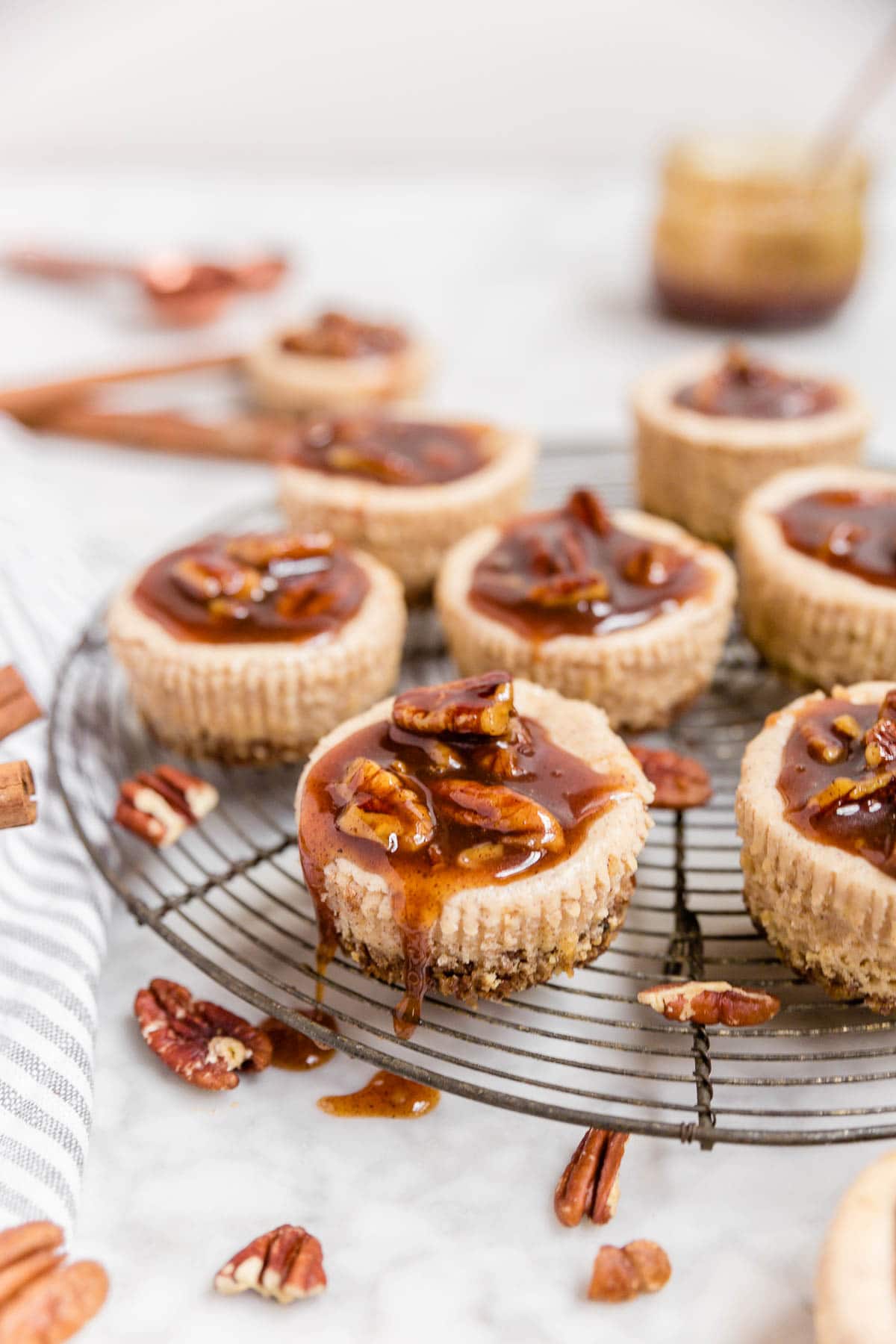 A cooling rack with mini pecan pie cheesecakes dripping with pecan pie caramel sauce ready for serving.