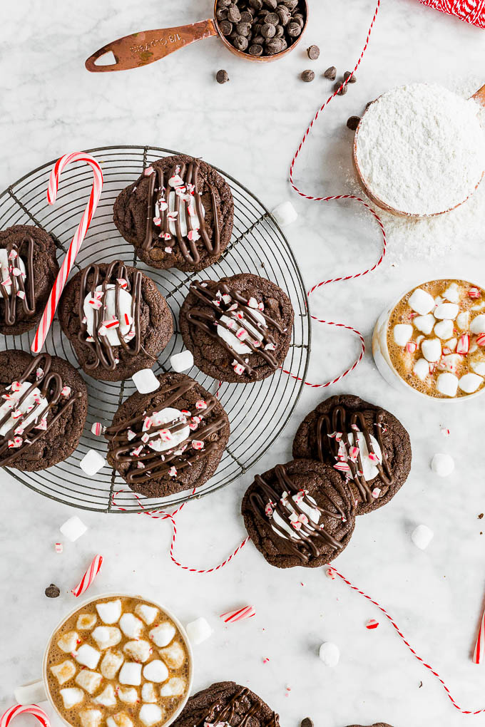 Gluten-Free Peppermint Hot Chocolate cookies on a cooling rack with two mugs of hot chocolate with mini marshsmallows and candy canes.