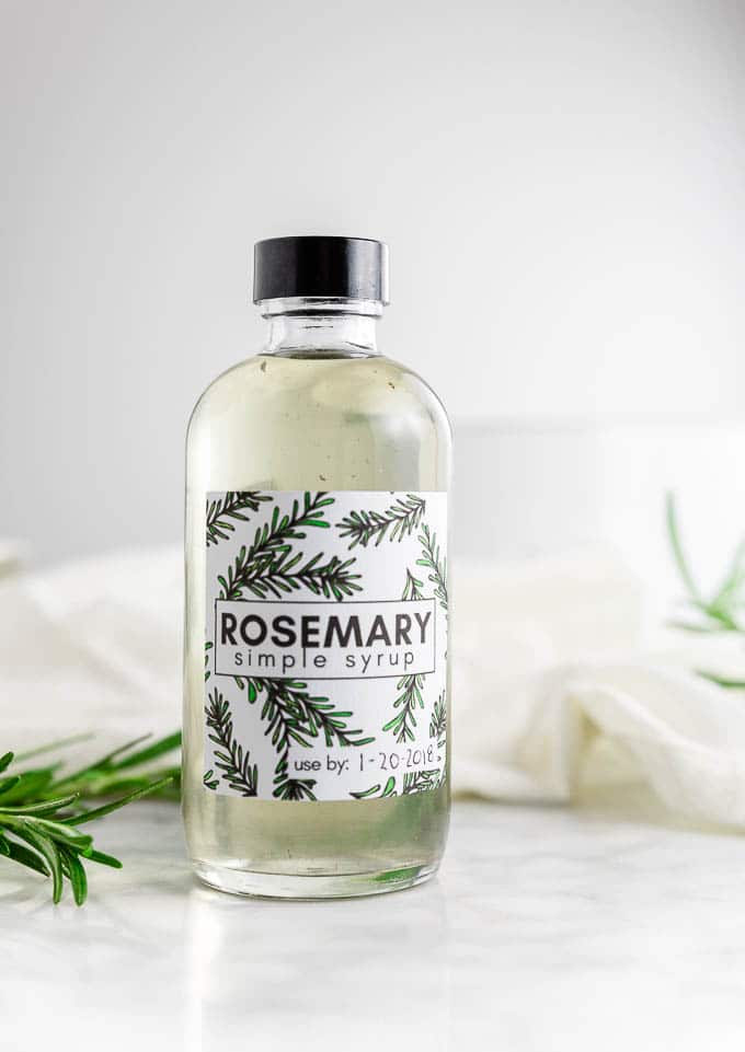 A bottle of rosemary simple syrup with fresh rosemary and sugar.