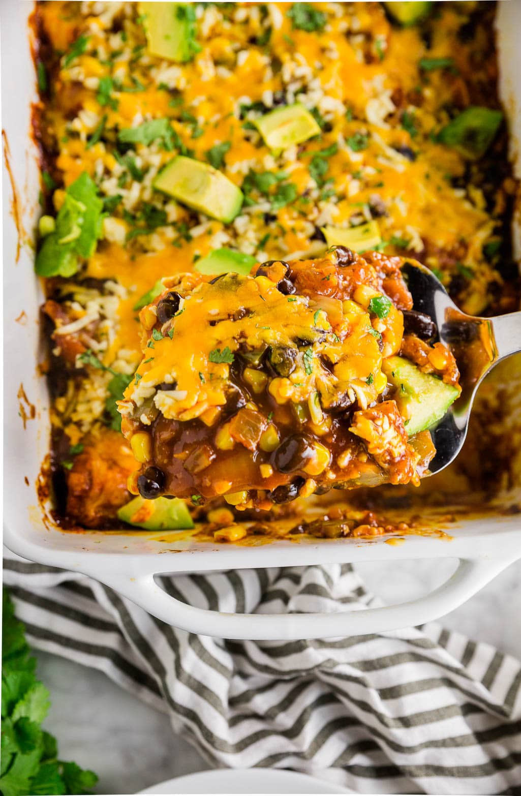 A metal spatula digging into a baking dish of gluten-free chicken enchilada casserole.
