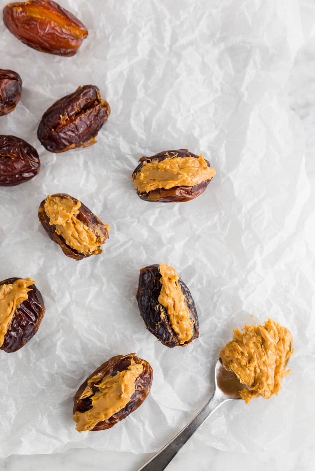 Peanut butter stuffed dates on a piece of parchment paper waiting to be dipped in chocolate.