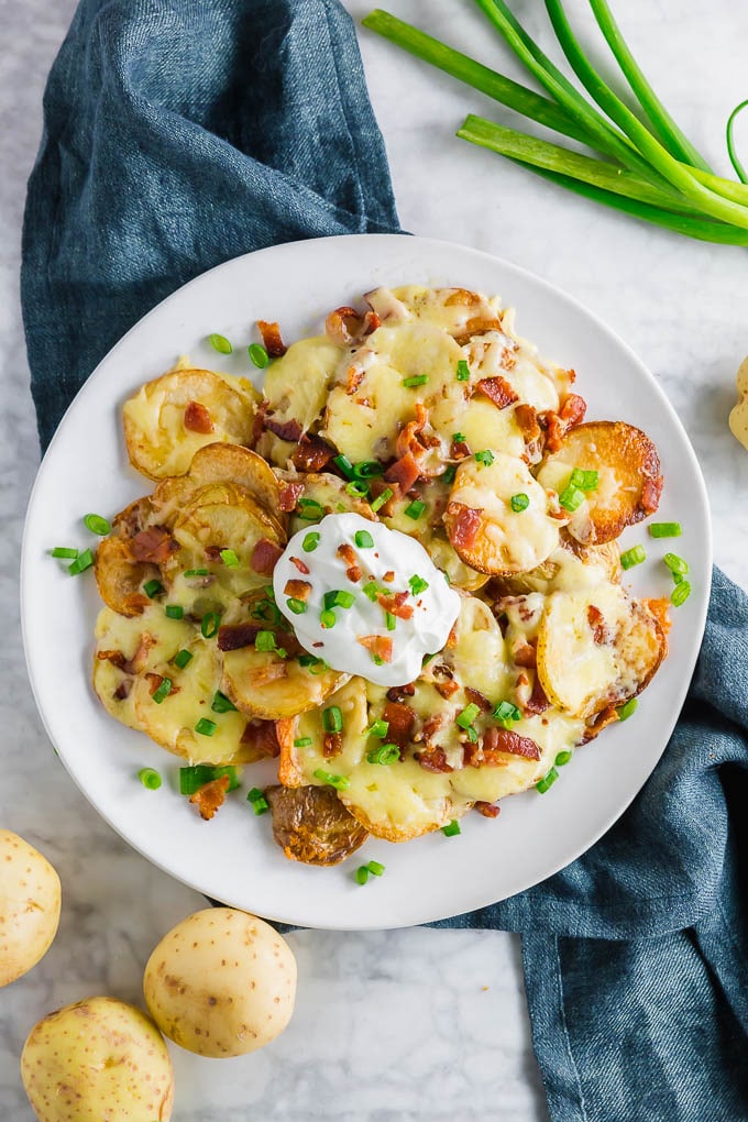 A plate of potato nachos with cheddar cheese, bacon, green onion and sour cream.