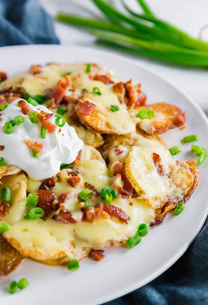 A photo of a plate of Irish Nachos with potatoes, cheddar cheese, bacon, sour cream and green onions.