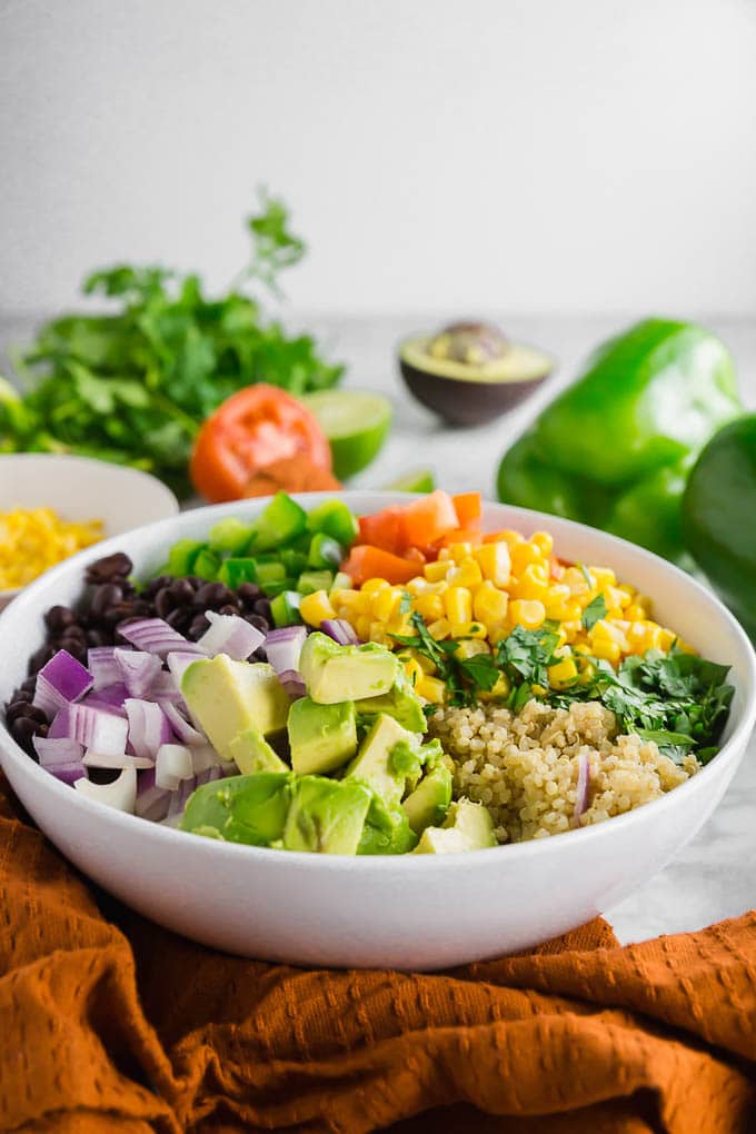 A bowl filled with quinoa, black beans, bell pepper, tomato, corn, cilantro, avocado and red onion.