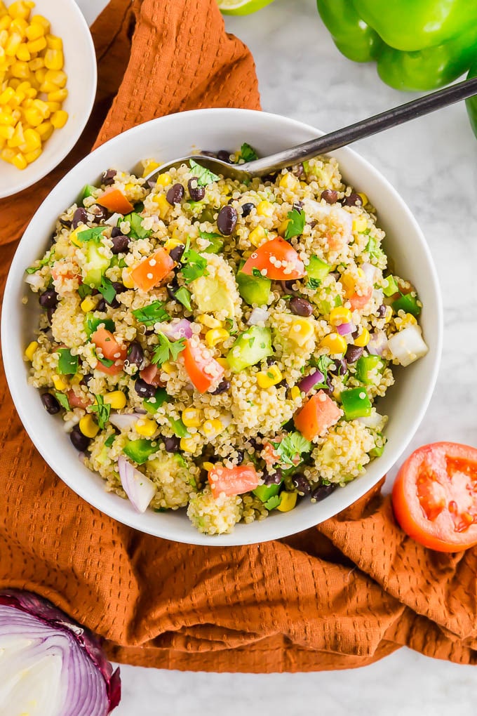 a bowl of southwest quinoa salad with tomatoes, avocado, red onion, cilantro, corn and black beans.