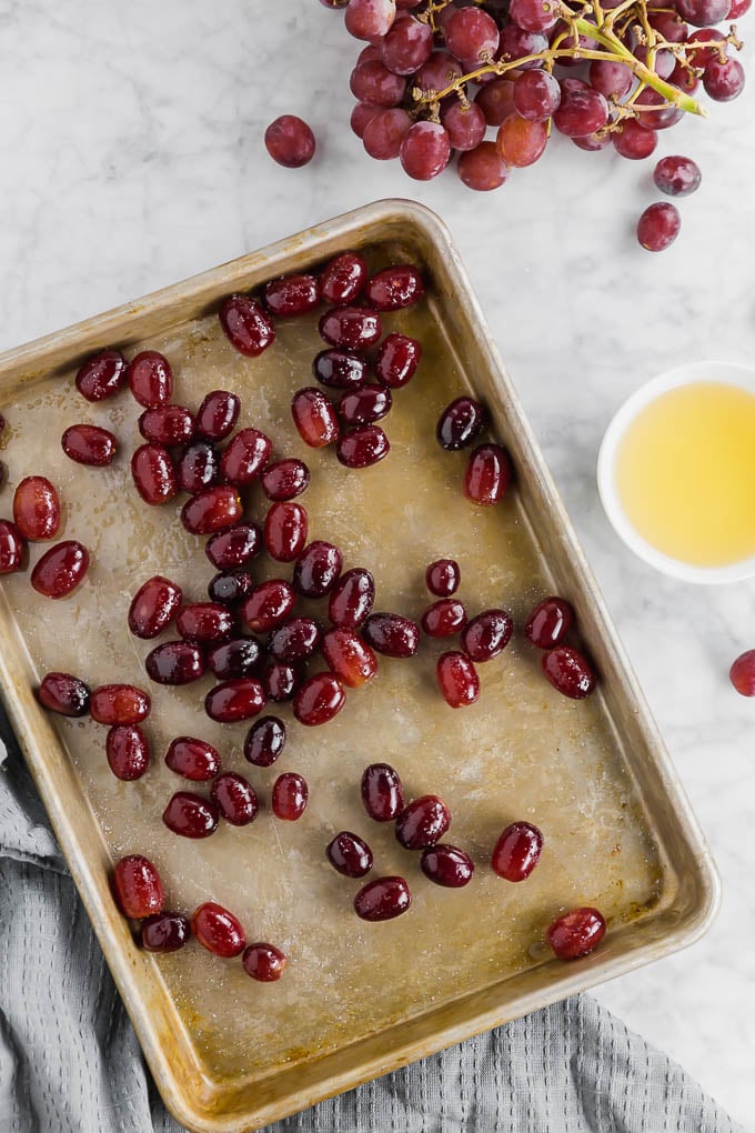 A baking sheet with red grapes tossed with avocado oil and salt ready to be roasted in the oven.