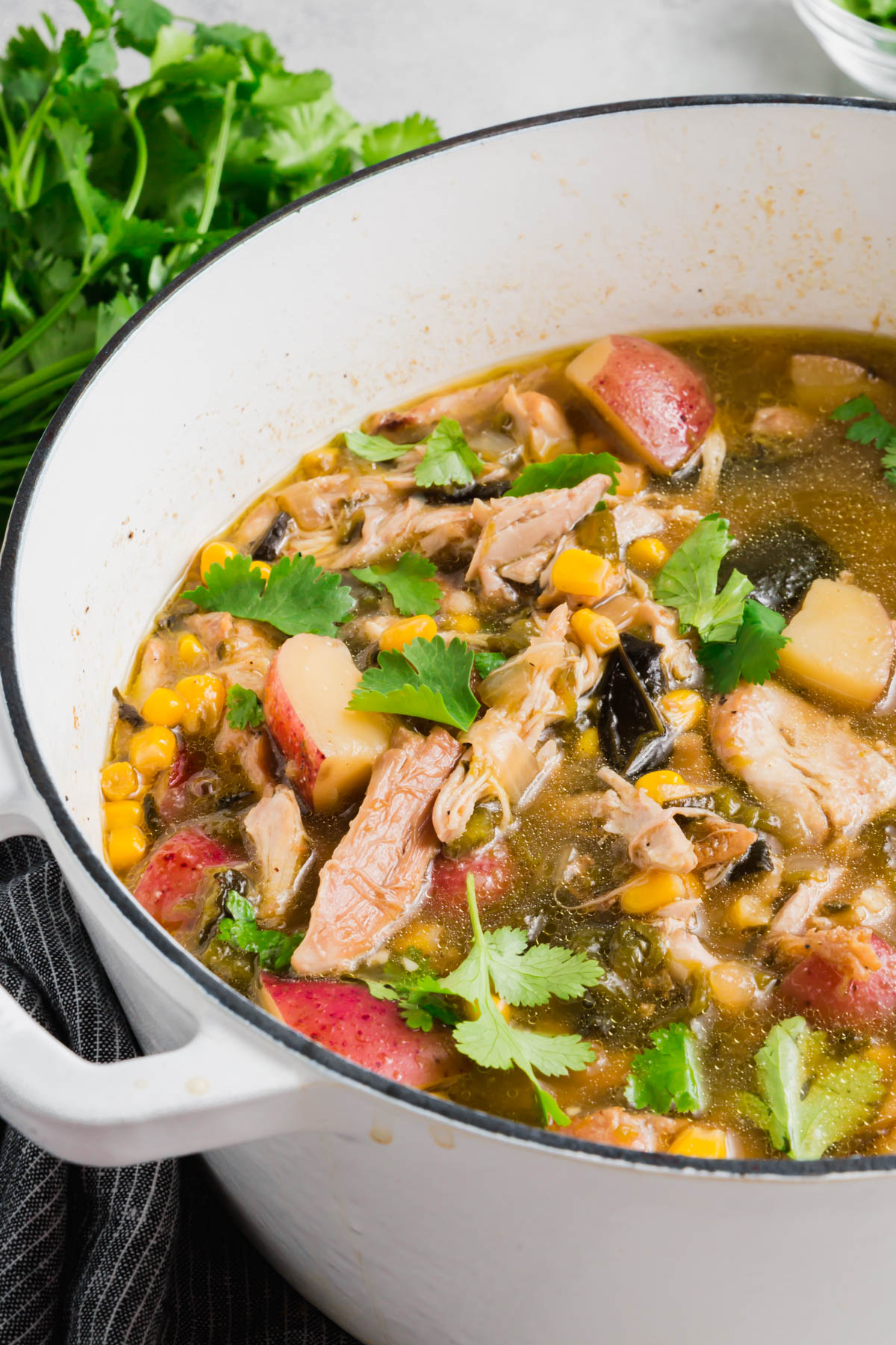 A white dutch oven with roasted poblano chicken soup topped with cilantro in it and a bunch of cilantro in the background.
