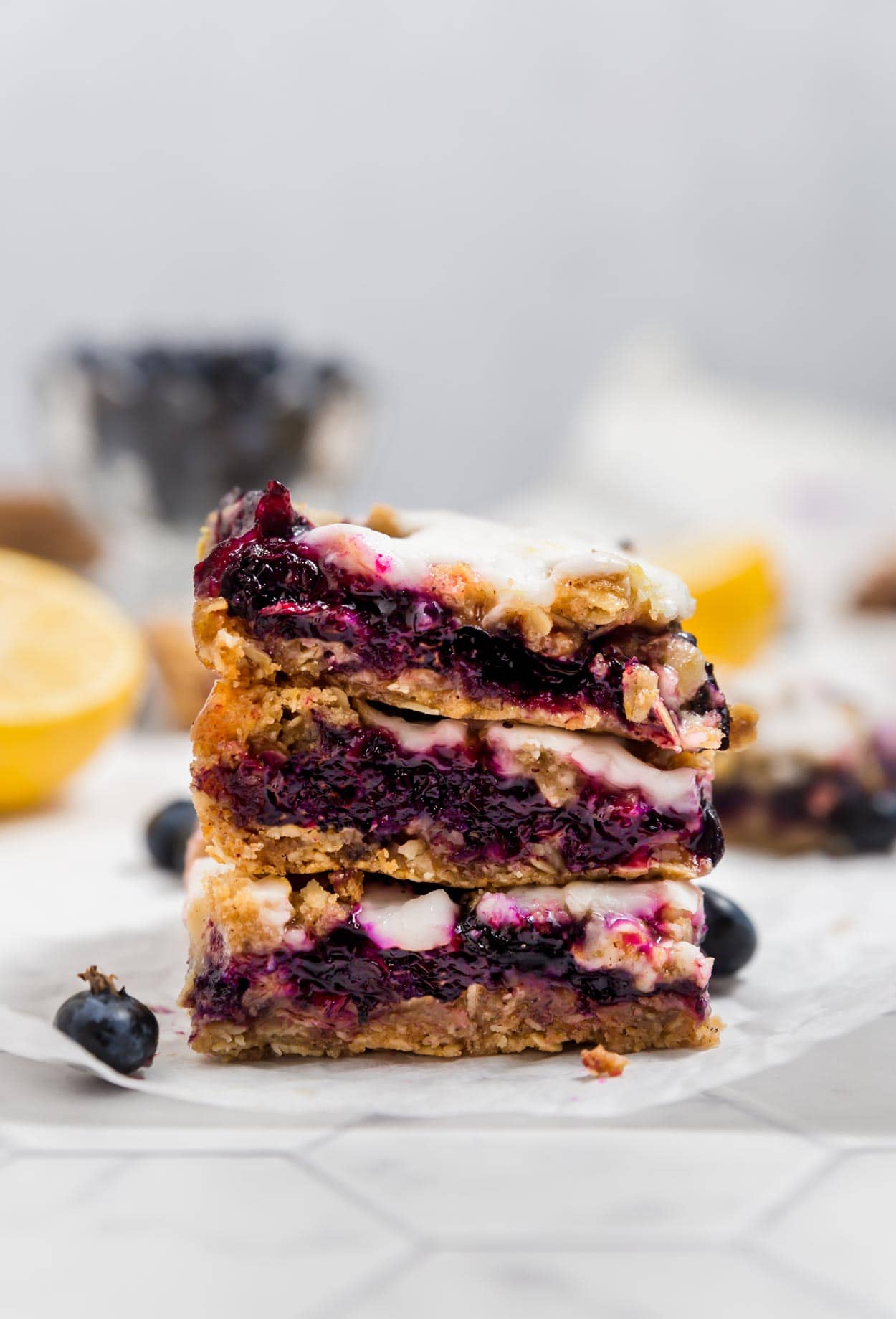 A stack of three blueberry crumb bars on top of each other with lemons and fresh blueberries in the background.