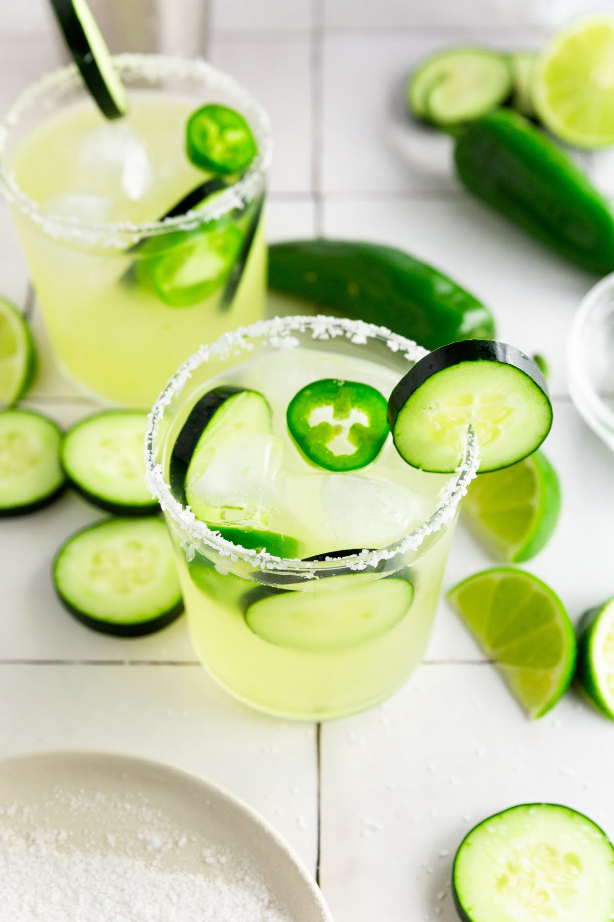 A photo of two margarita glasses filled with cucumber jalapeño margarita and rimmed with kosher salt.