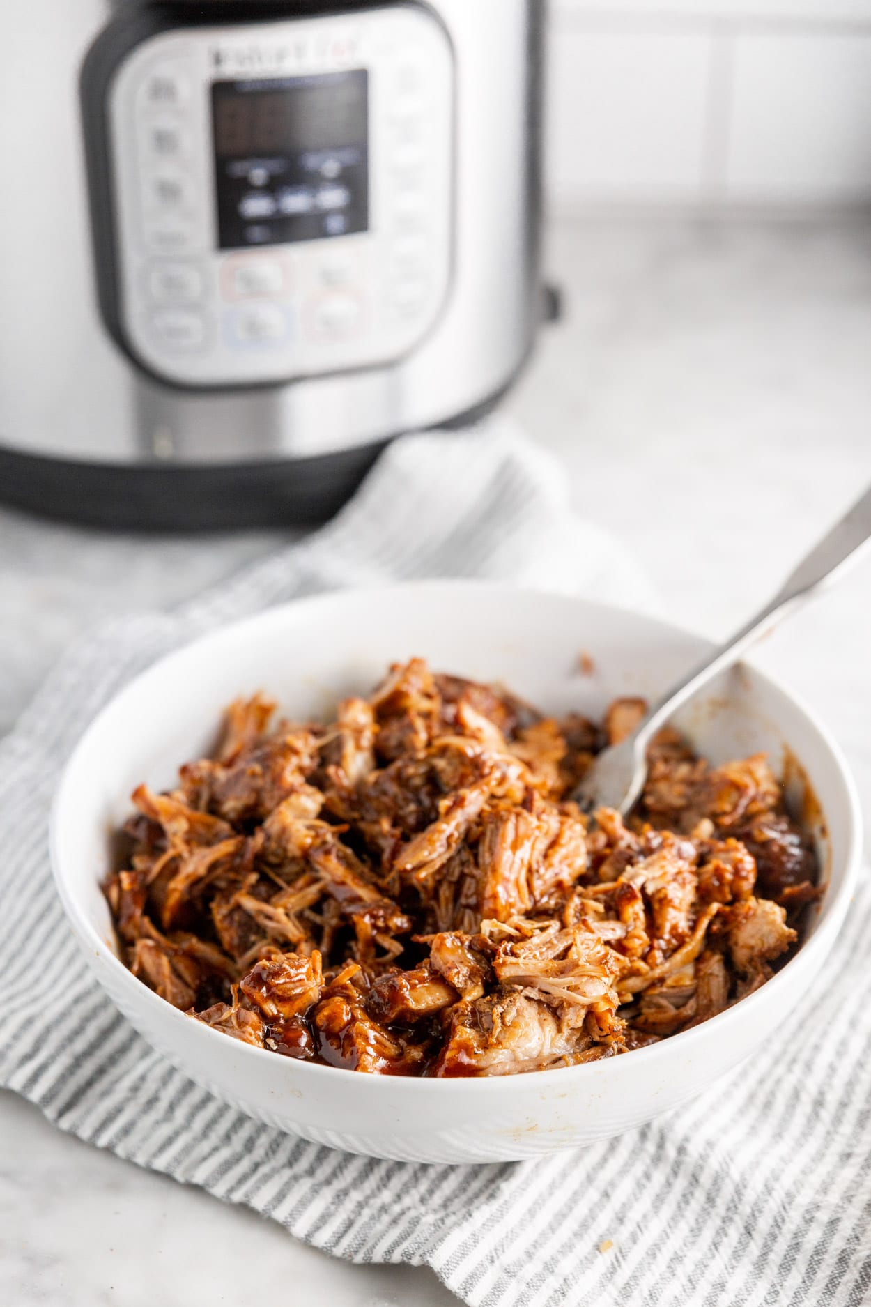 A bowl of shredded BBQ pulled pork in a bowl with an Instant Pot in the background.