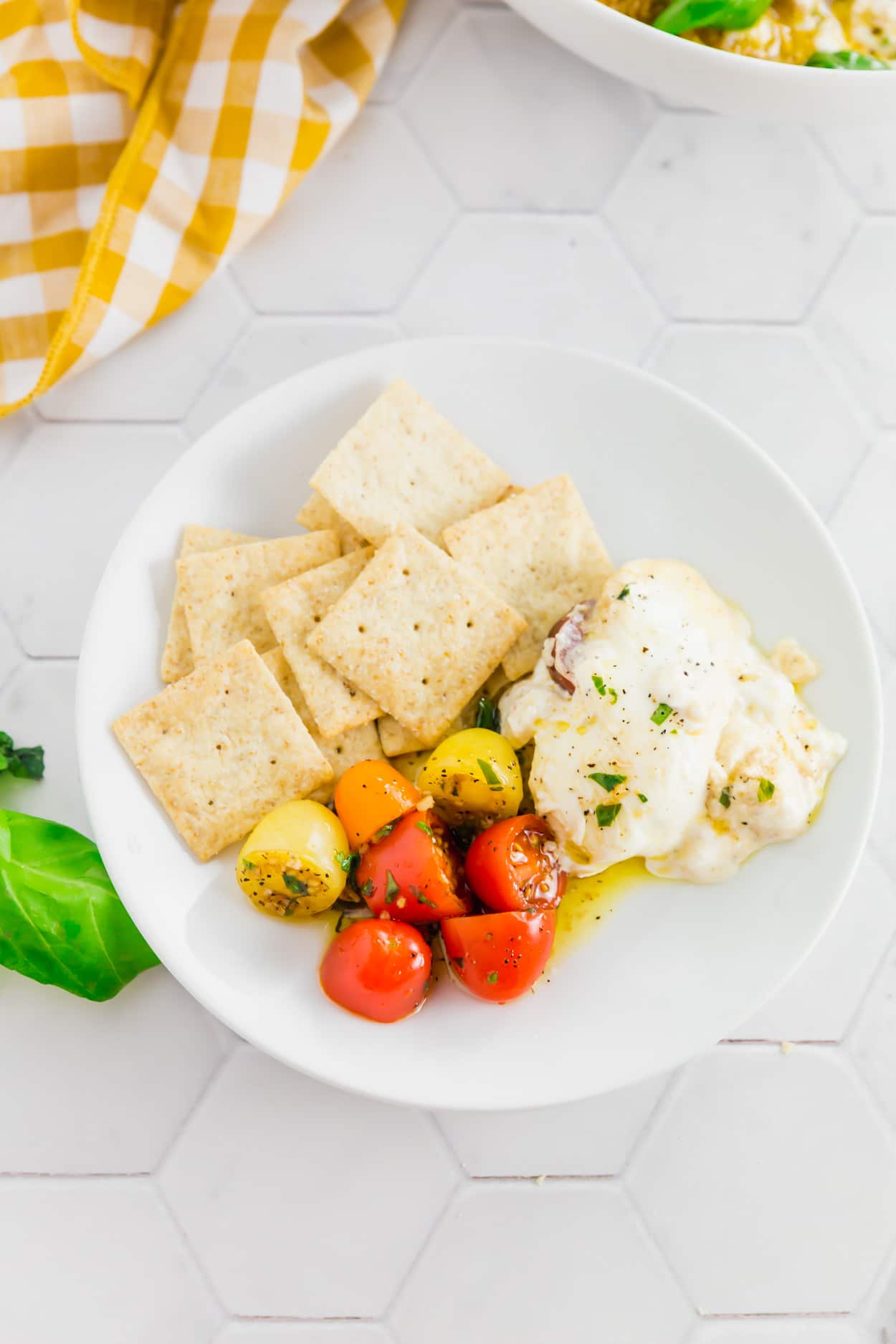 An overhead photo of a plate with gluten-free crackers served with marinated tomatoes and creamy burrata.