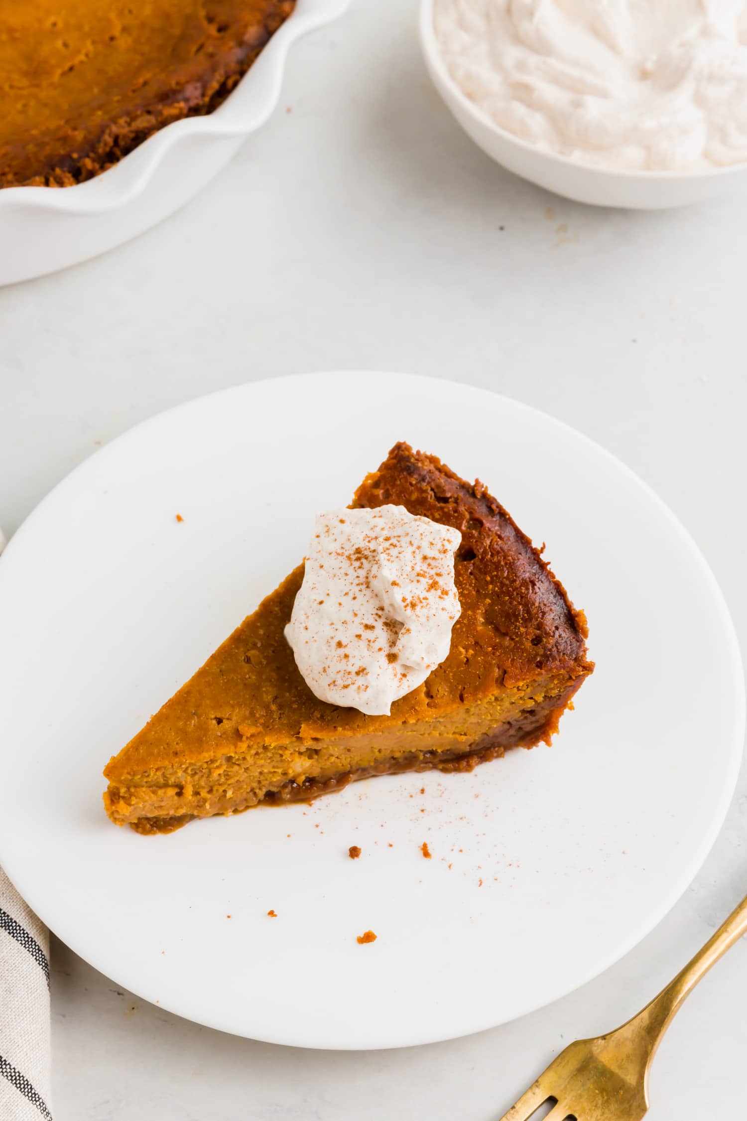 An overhead photo of a slice of pumpkin pie with gluten free graham cracker crust and a dollop of whipped cream.