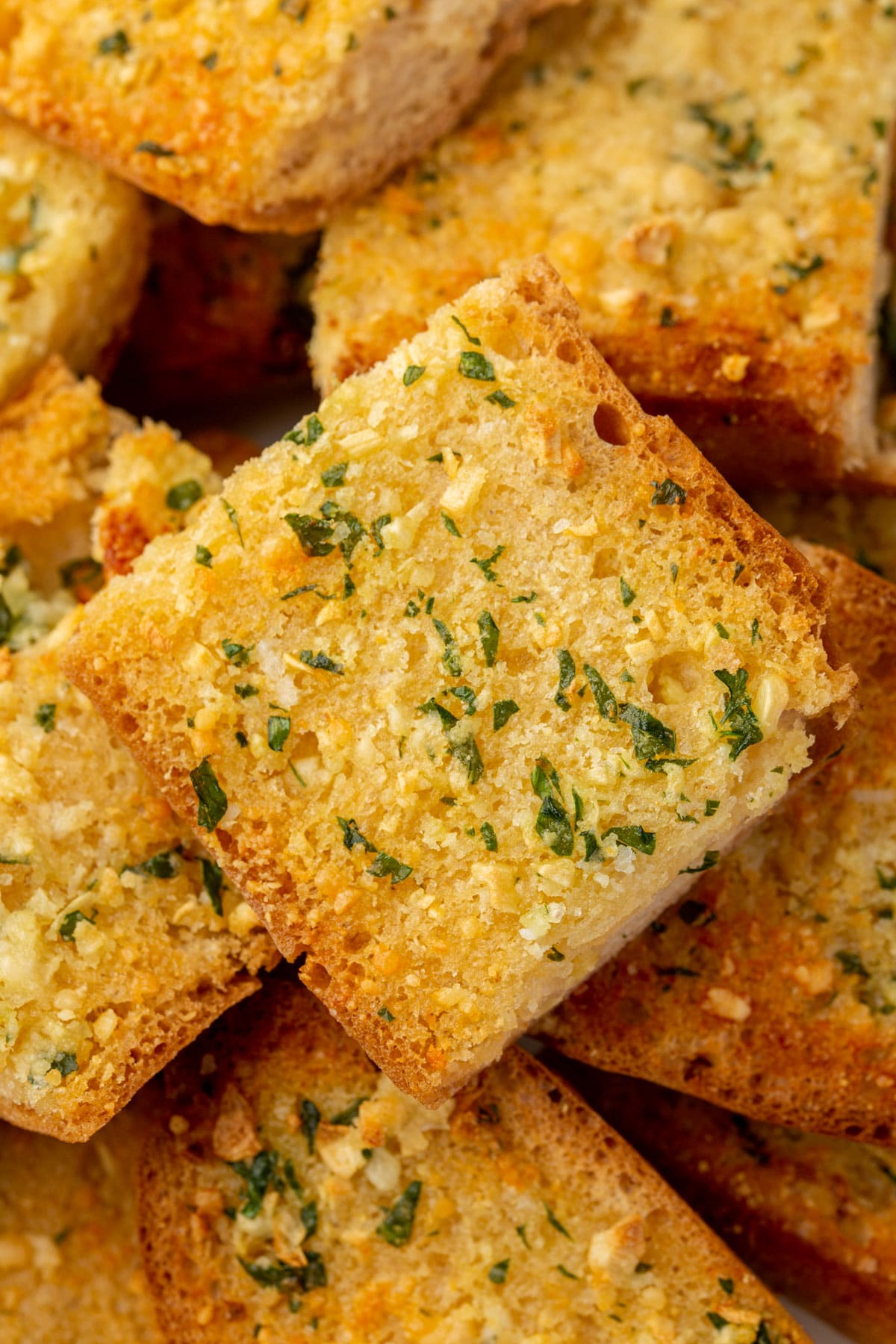 Close up photo of garlic bread slices, showing the golden butter and herbs in a serving bowl.