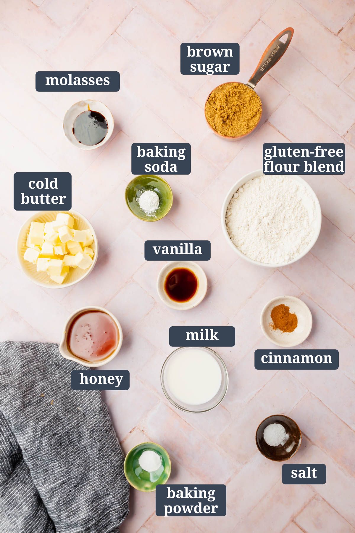 Ingredients in small bowls on a table to make gluten-free graham crackers with labels over them.