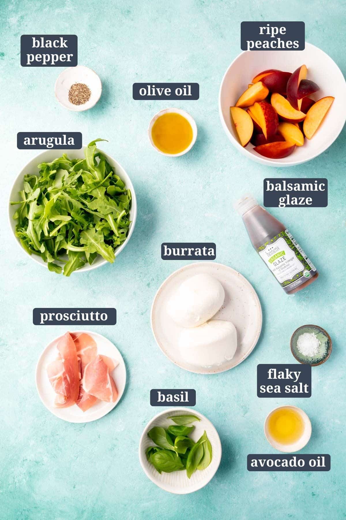 Ingredients in small bowls to make grilled peach burrata salad with text overlays including black pepper, olive oil, ripe peaches, arugula, burrata, balsamic glaze, prosciutto, burrata, flaky sea salt, avocado oil, and basil.