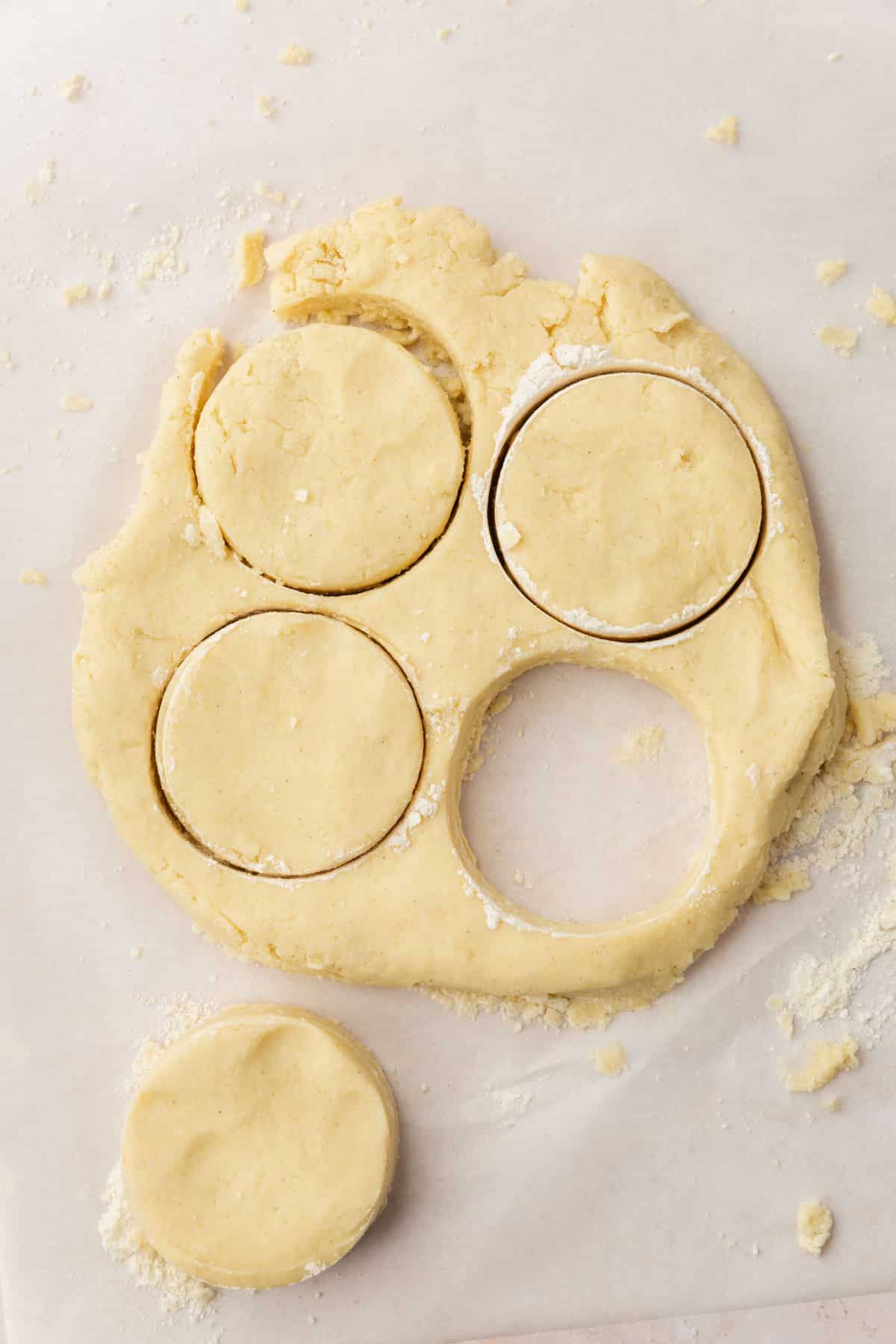 A rolled out square of gluten-free biscuit dough with 3 round biscuits cut out of it.