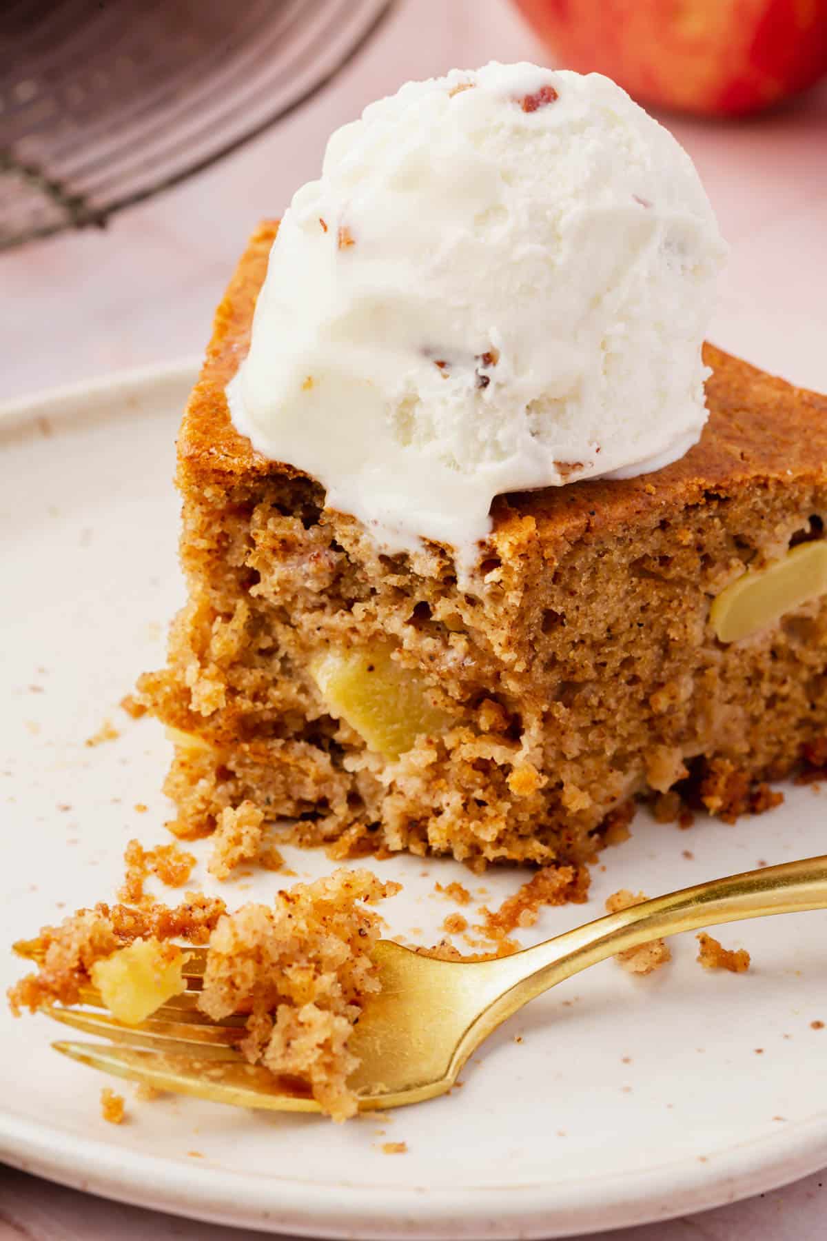 A wedge of gluten-free apple cake topped with a scoop of ice cream with a bite taken out of it.