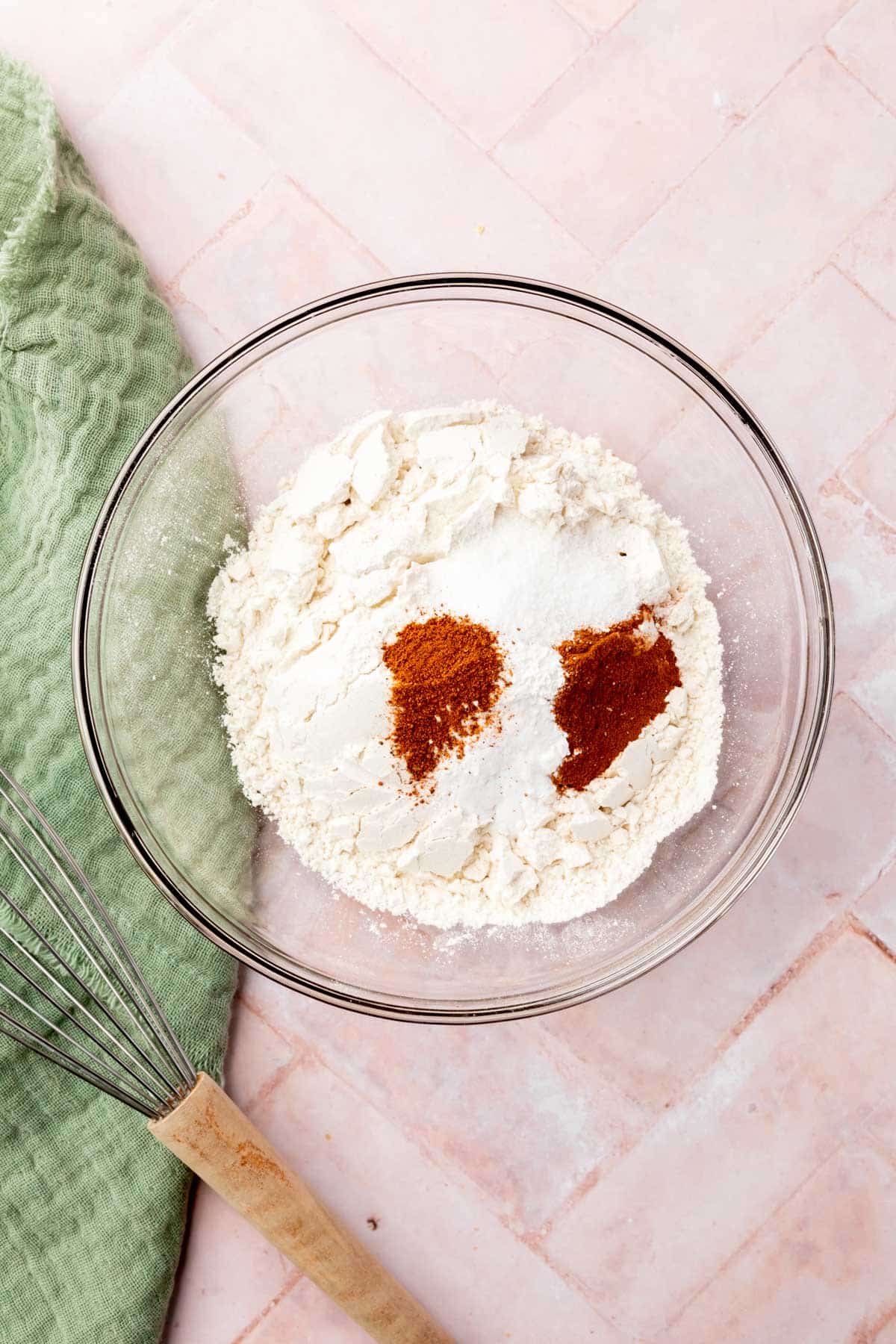 A glass mixing bowl with gluten-free flour blend, salt, cinnamon, baking soda, baking powder, and nutmeg in it before mixing.