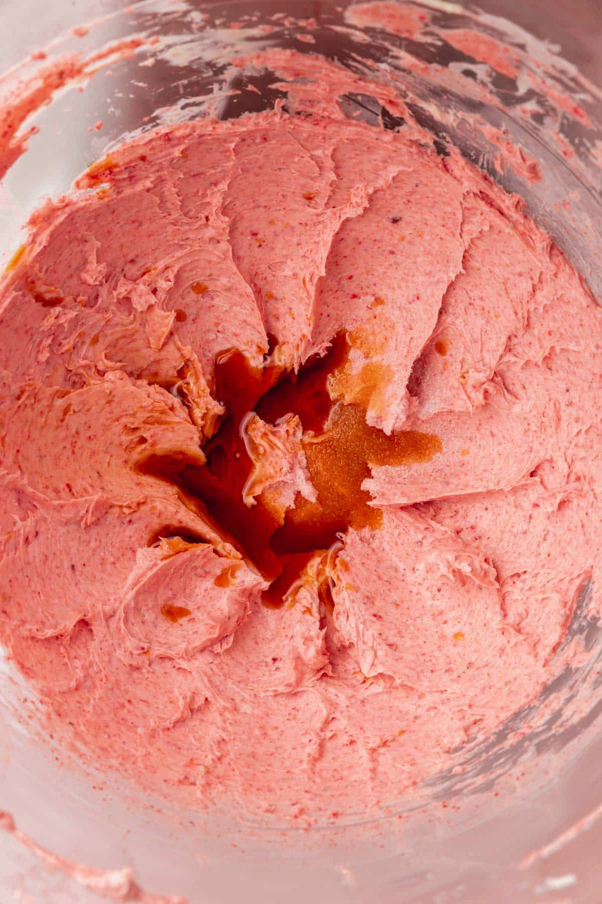Creamed butter and freeze-dried strawberries topped with vanilla extract in the bowl of a stand mixer.
