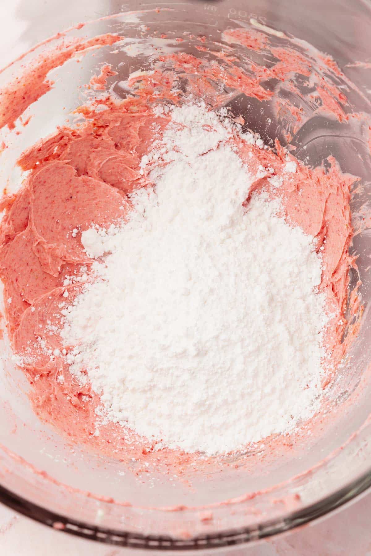 Creamed butter and freeze-dried strawberries topped with powdered sugar in the bowl of a stand mixer.