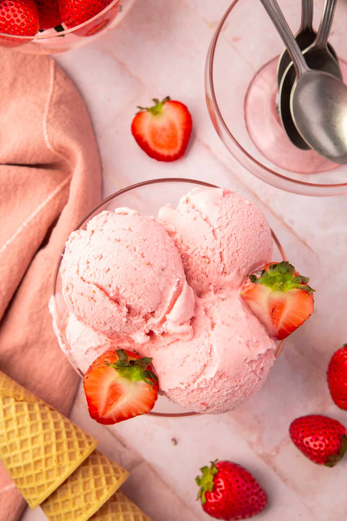 An overhead view of a glass bowl with scoops of strawberry ice cream topped with strawberry halves.