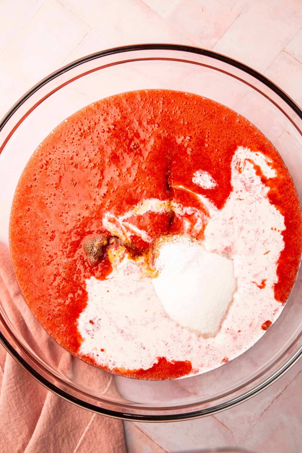 A glass bowl with pureed strawberries, heavy cream, vanilla extra and granulated sugar in it.
