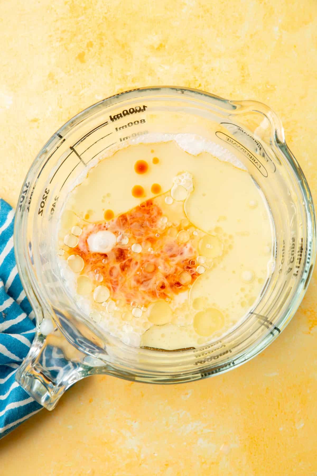 A glass measuring cup filled with almond milk, applesauce, vanilla, and oil that has not yet been mixed together.