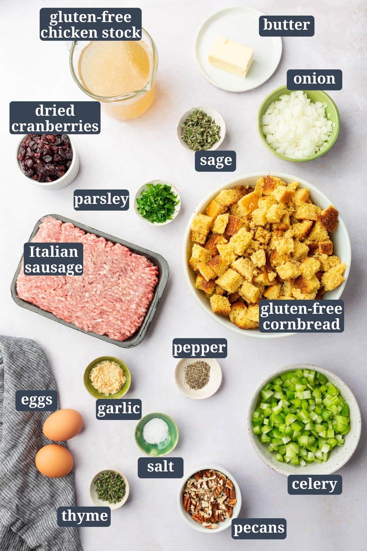 Ingredients in small bowls on a table to make gluten-free cornbread stuffing, including chicken stock, dried cranberries, cornbread, celery, pepper, pecans, salt, garlic, thyme, sage, butter, parsley, Italian sausage, onion, and eggs with text overlays over each image.