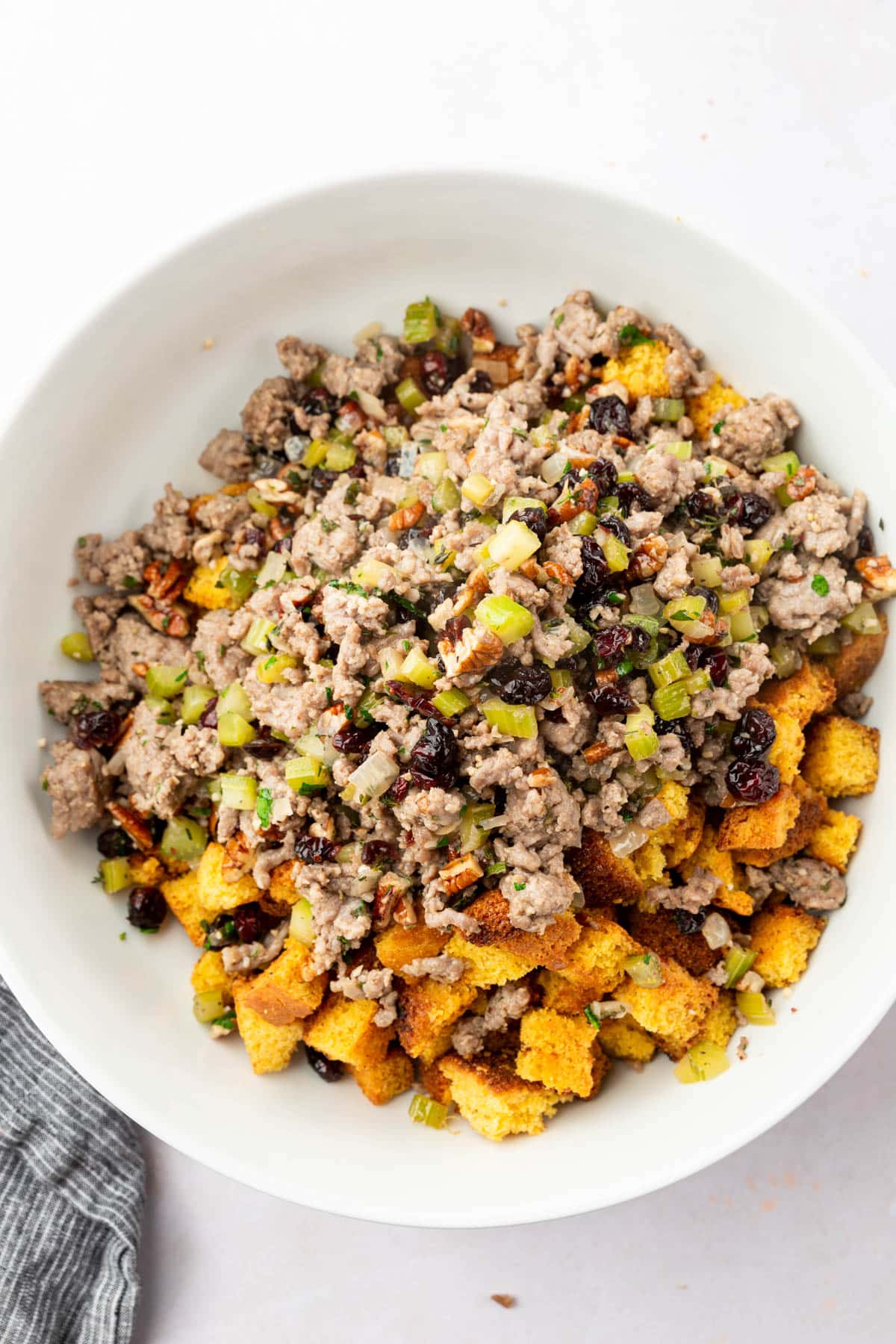 A large mixing bowl of cornbread cubes, Italian sausage, celery, pecans, cranberries, onions, thyme, sage, eggs, and chicken stock.