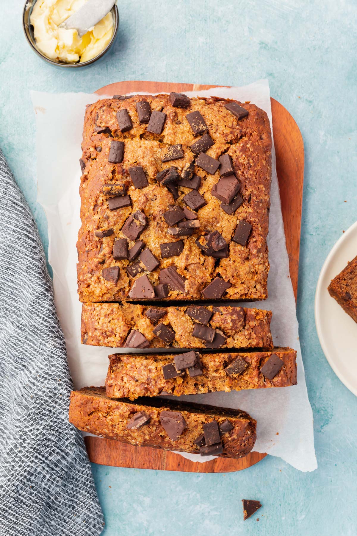 An overhead view of a loaf of gluten-free vegan chocolate chunk banana bread on a wood cutting board that has been partially sliced.