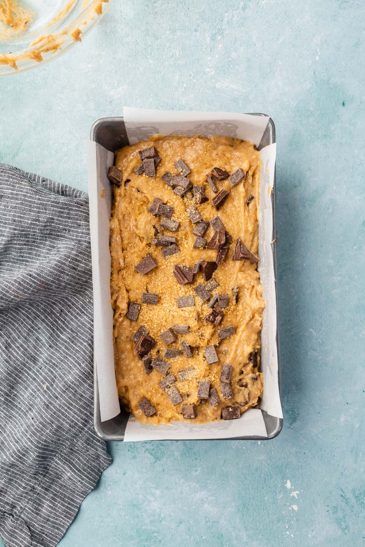 An overhead view of gluten-free banana bread batter topped with chocolate chunks and turbinado sugar before baking.
