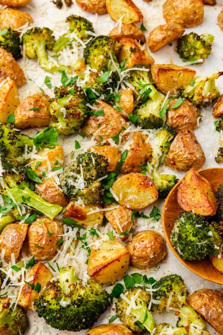 Roasted broccoli and potatoes topped with parsley and shredded parmesan cheese on a baking sheet with a wood spoon.