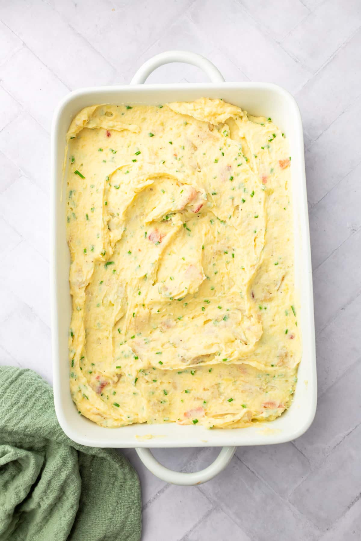 A casserole dish filled with mashed potatoes mixed with chopped chives and bacon bits.