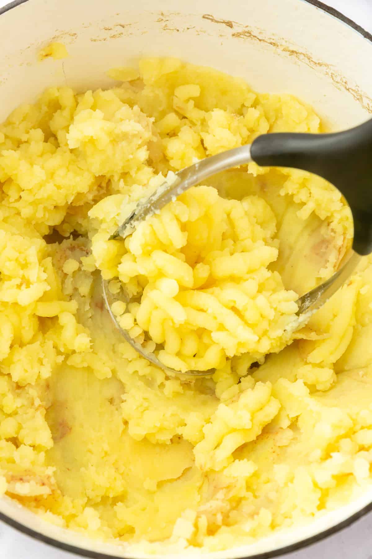 A potato masher mashing potatoes in a large dutch oven.