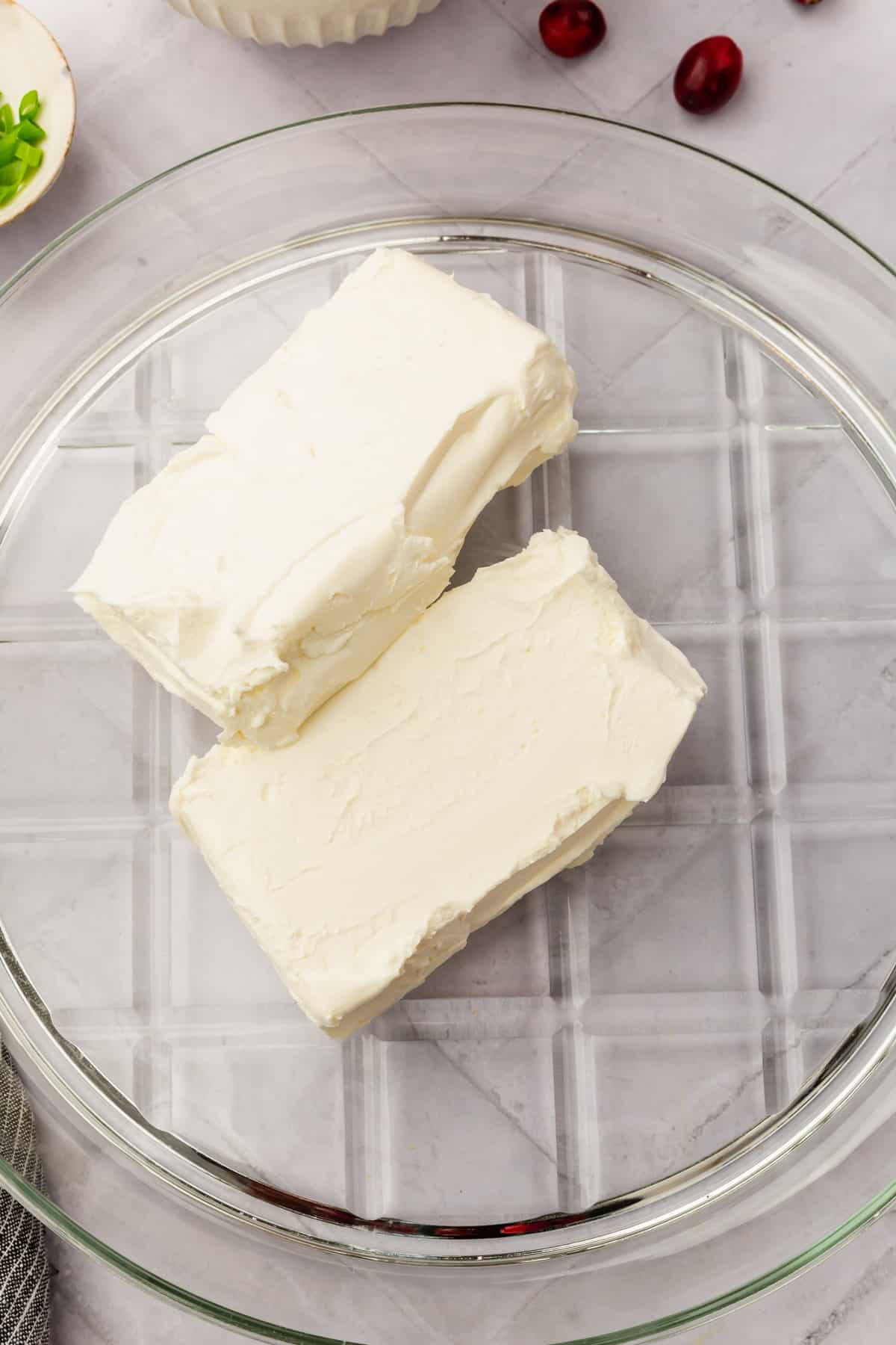 Two bricks of cream cheese on a clear serving platter.