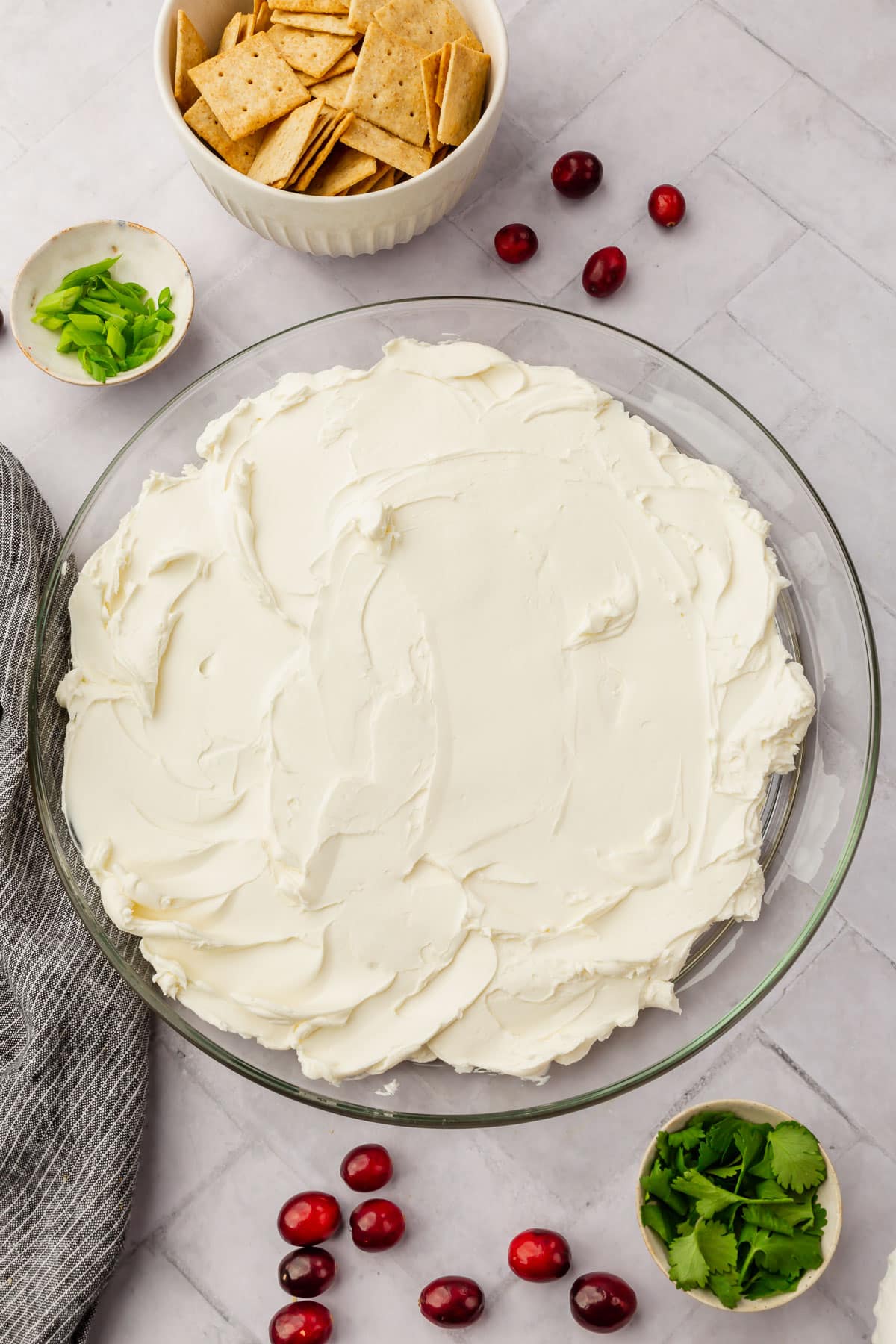 A clear platter with softened cream cheese smeared all over the top of it, with bowls of cilantro, gluten-free crackers and green onions on the side.