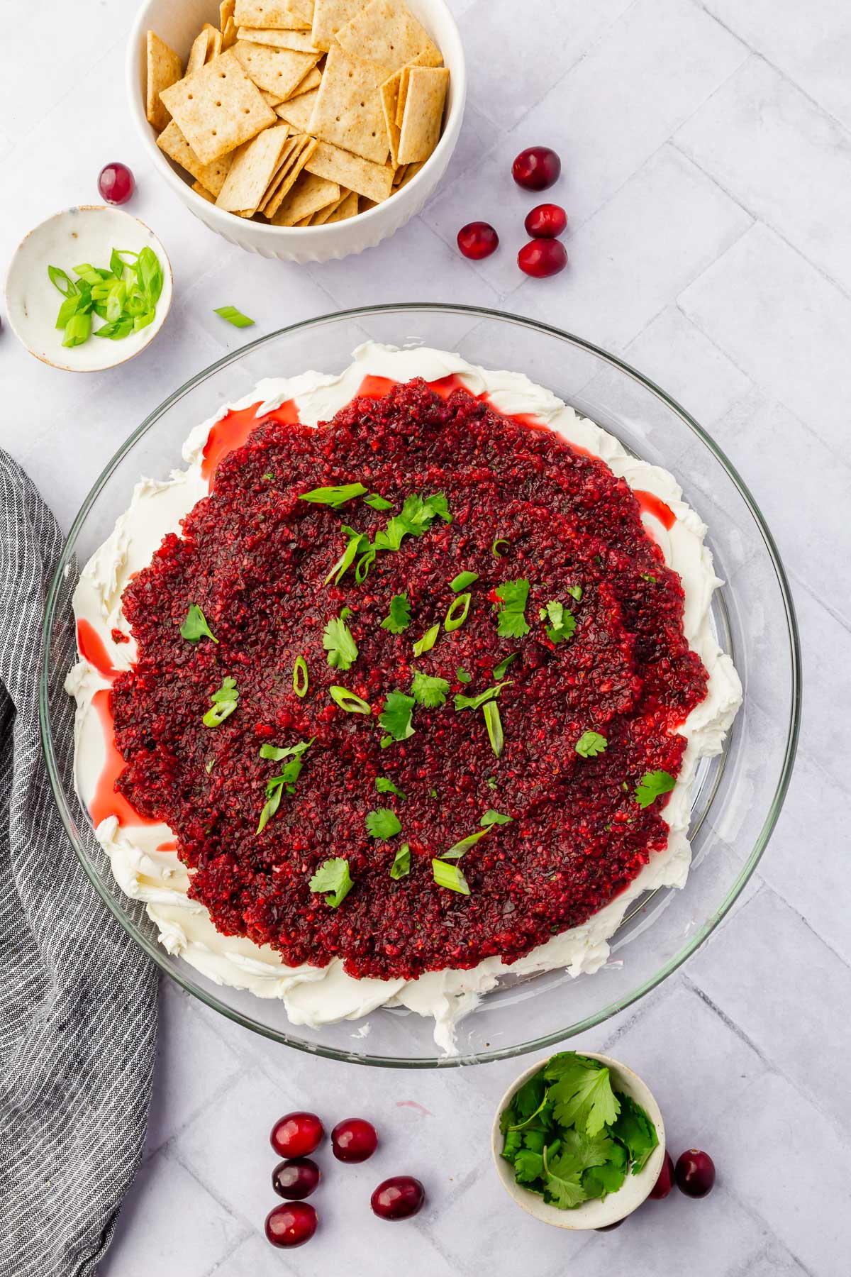 A platter of cream cheese topped with cranberry salsa, green onion and cilantro with gluten-free crackers on the side.