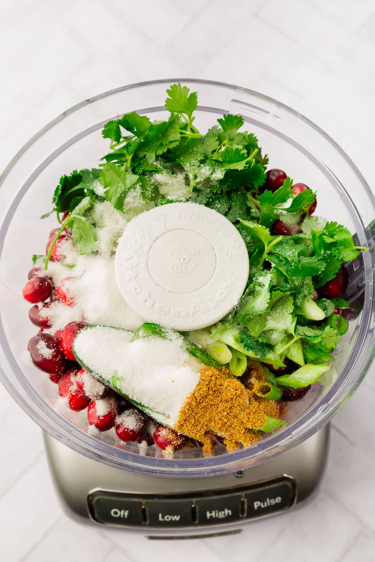 A food processor with cranberries, jalapeño, cilantro, green onions, sugar, cumin and lime juice.