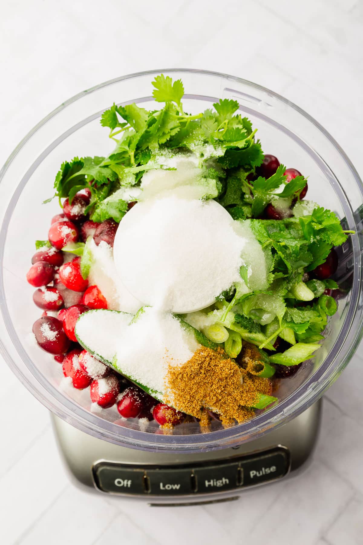 A food processor with cranberries, jalapeño, cilantro, green onions, sugar, cumin and lime juice.