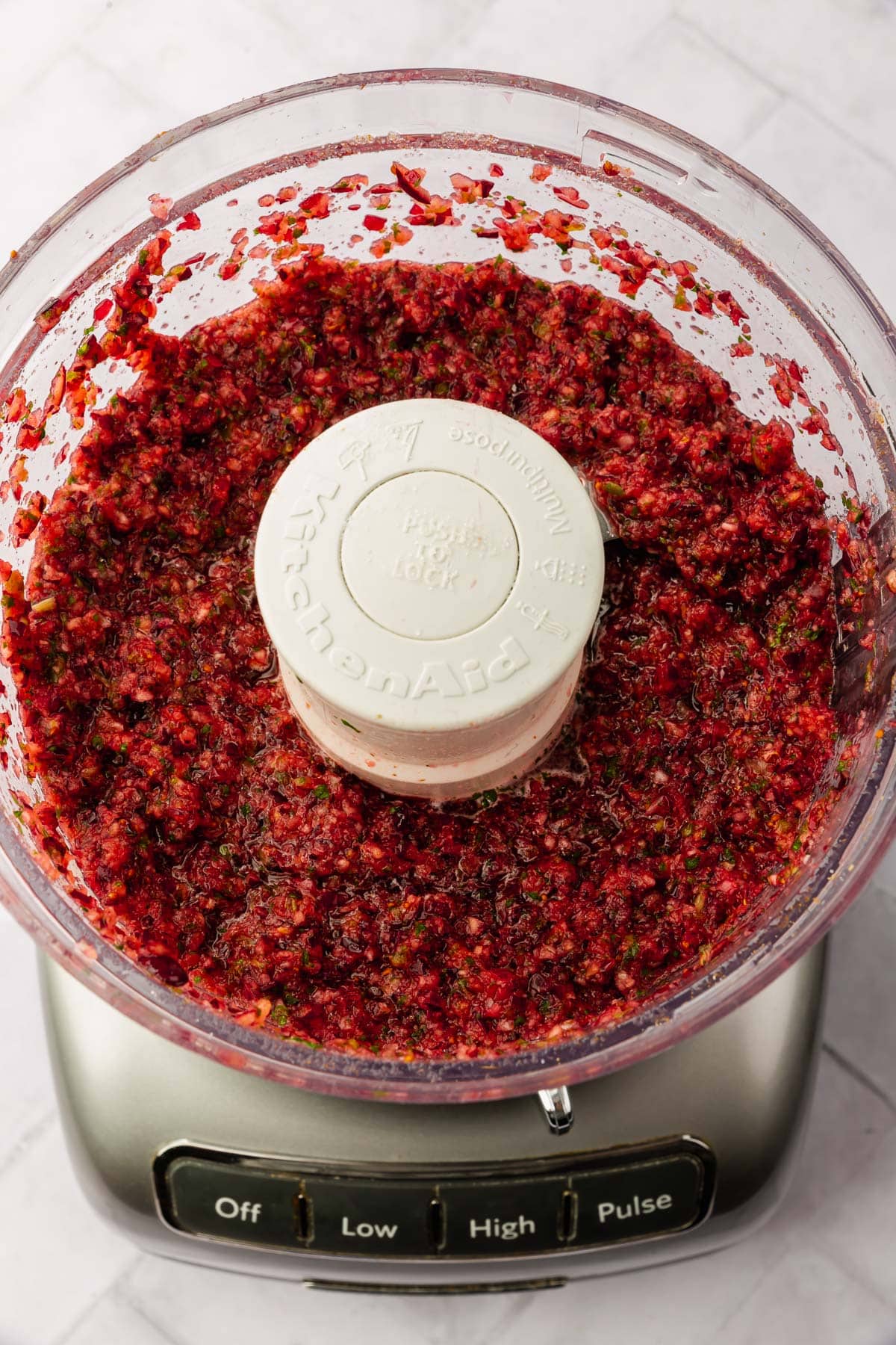 A food processor with cranberry jalapeño salsa in it that has been pulsed until finely chopped.