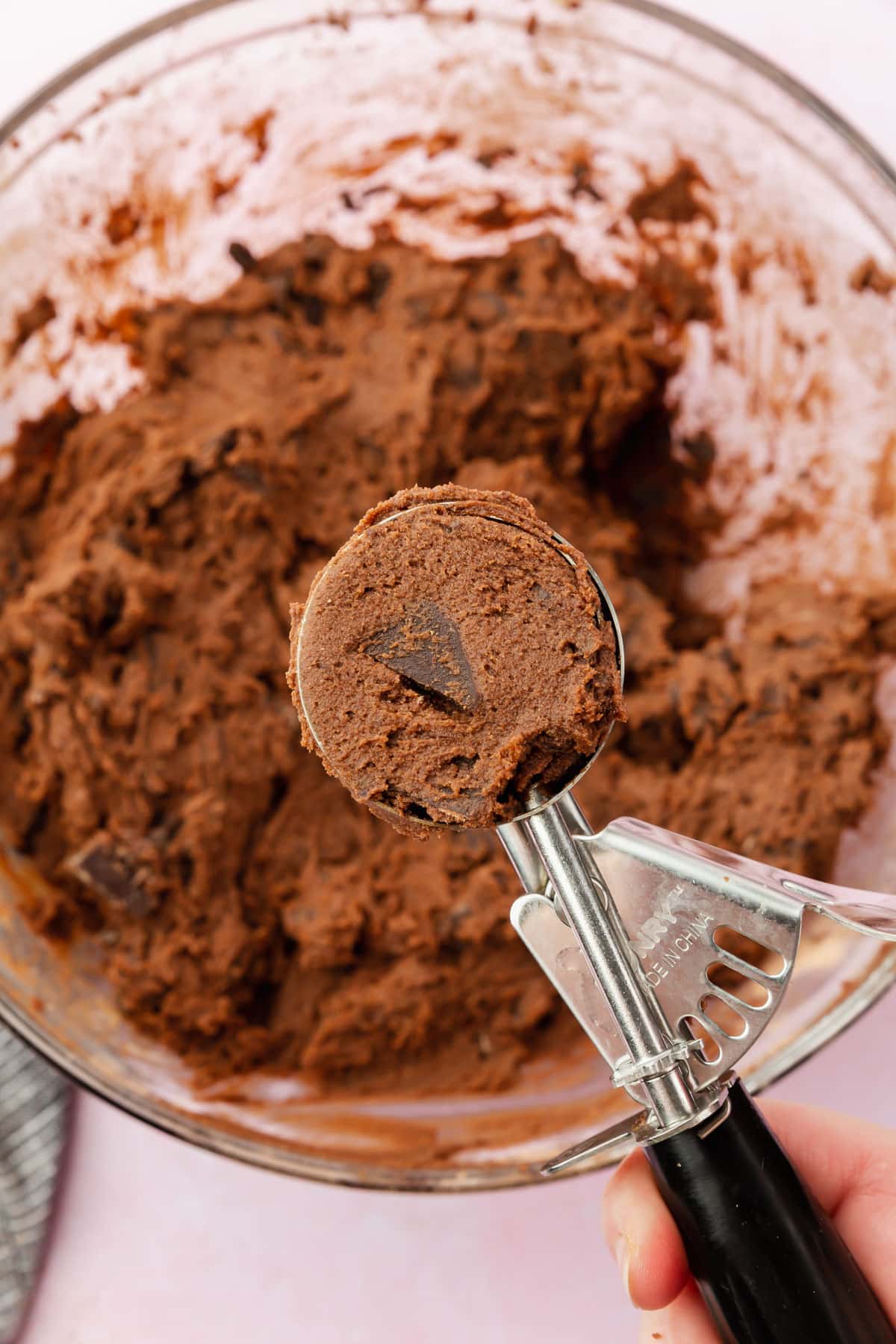 A cookie scoop filled with gluten-free chocolate chunk cookie dough over a bowl of more cookie dough.