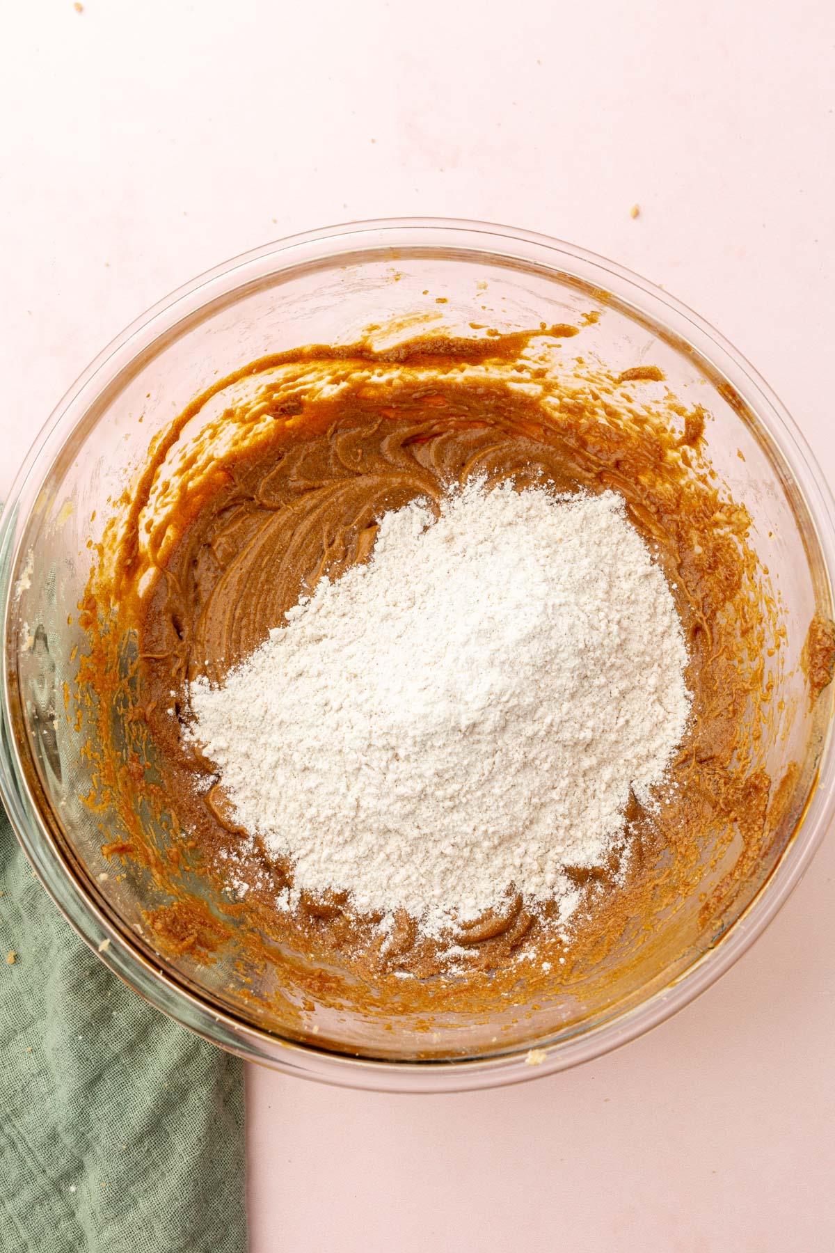 A glass mixing bowl with gluten-free gingerbread wet ingredients with a gluten-free flour blend on top.