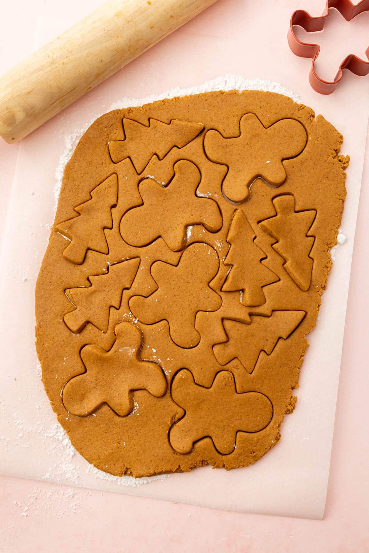 Gluten-free gingerbread cookie dough rolled out on parchment paper with gingerbread men and Christmas trees cut out of them.